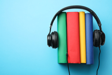 Photo of Books and modern headphones on light blue background, top view. Space for text