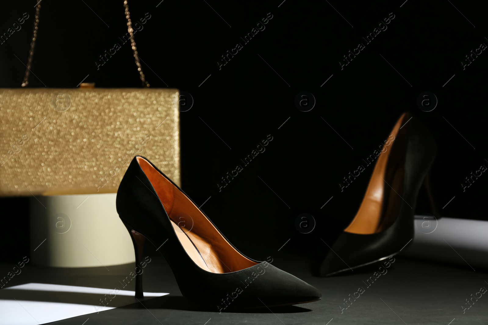 Photo of Pair of elegant high heel shoes and clutch on black background