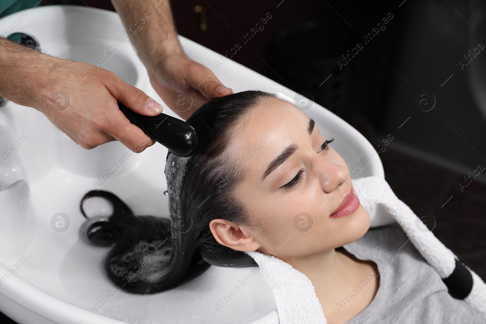 Photo of Stylist washing client's hair at sink in beauty salon