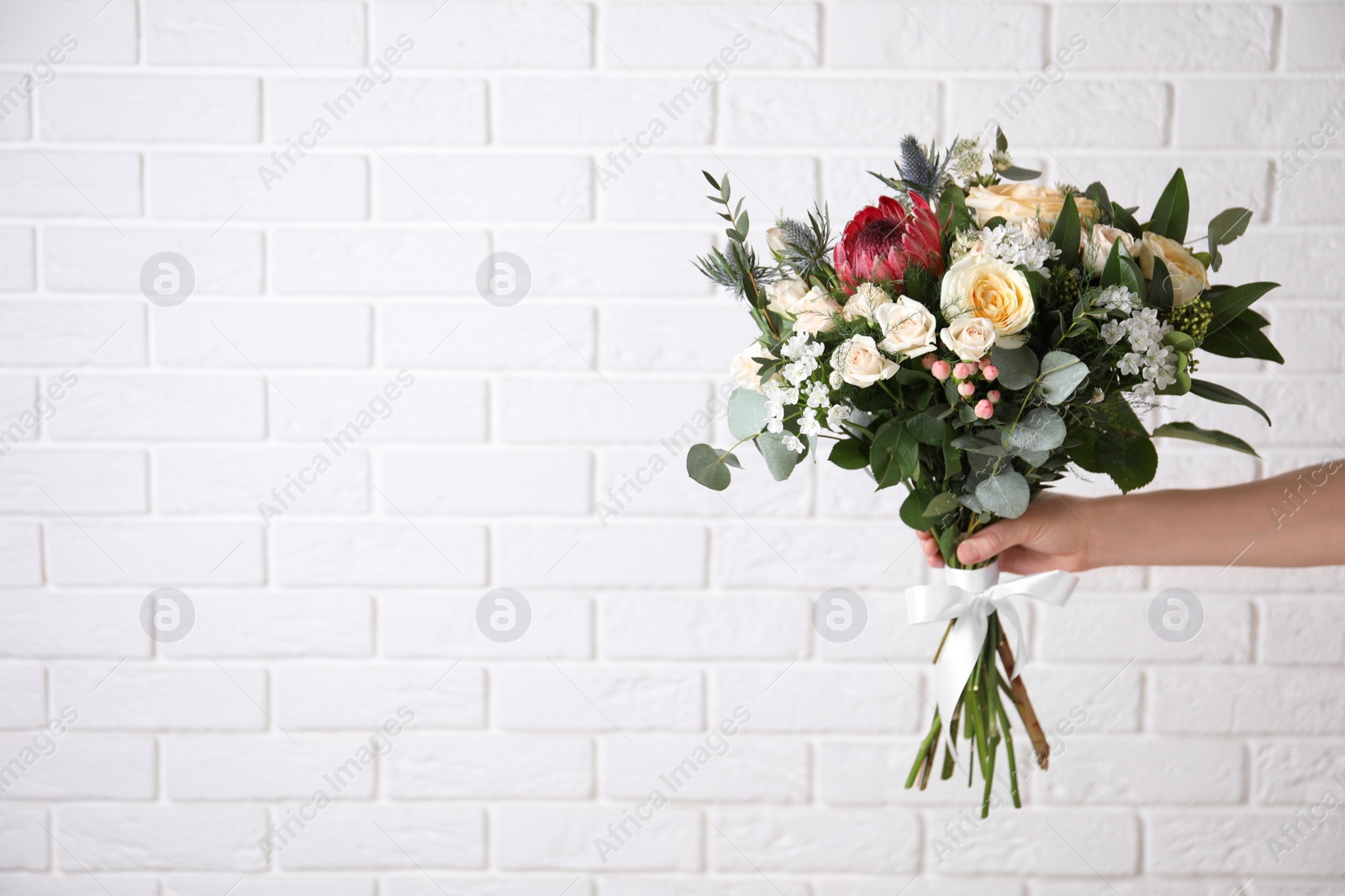 Photo of Woman with bouquet of beautiful roses near white brick wall, closeup. Space for text