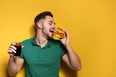 Photo of Handsome man with tasty burger and cola on color background. Space for text