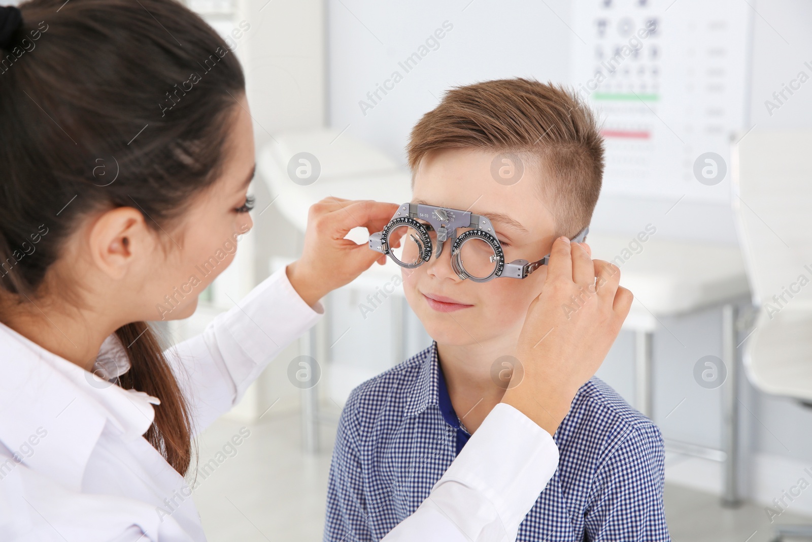 Photo of Children's doctor putting trial frame on little boy in clinic. Eye examination