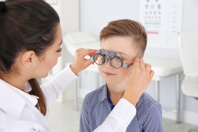 Photo of Children's doctor putting trial frame on little boy in clinic. Eye examination