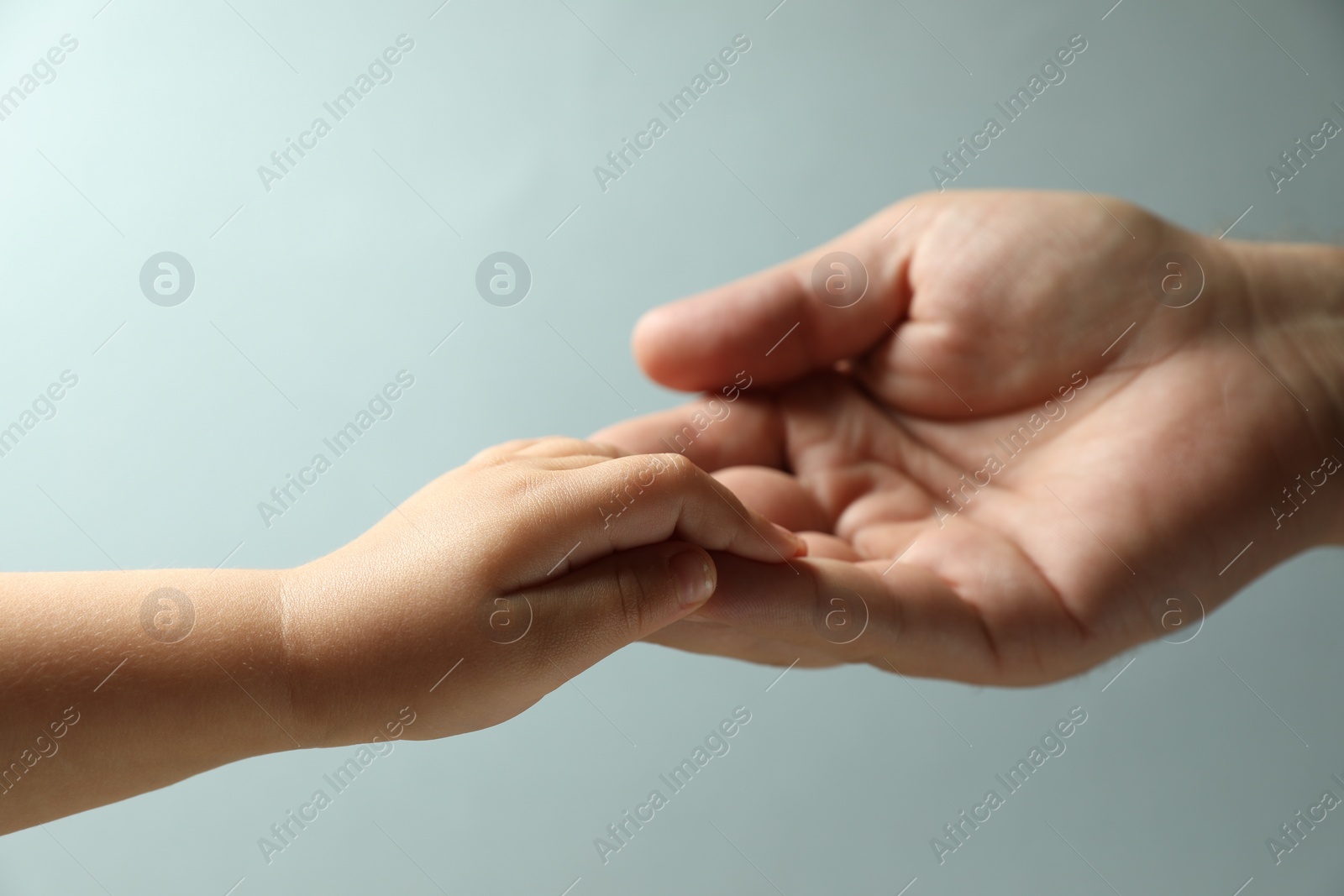 Photo of Father and child holding hands on light blue background, closeup