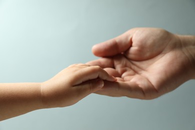 Father and child holding hands on light blue background, closeup