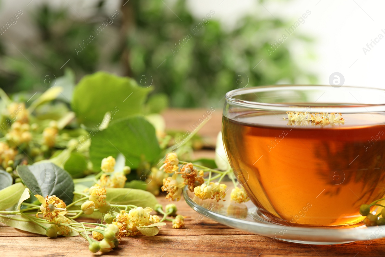 Photo of Cup of tea and linden blossom on wooden table, closeup