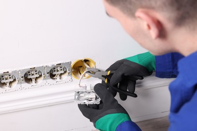 Photo of Professional repairman fixing power sockets with pliers indoors, closeup