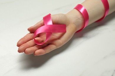 Photo of Woman with pink ribbon at white marble table, closeup. Breast cancer awareness