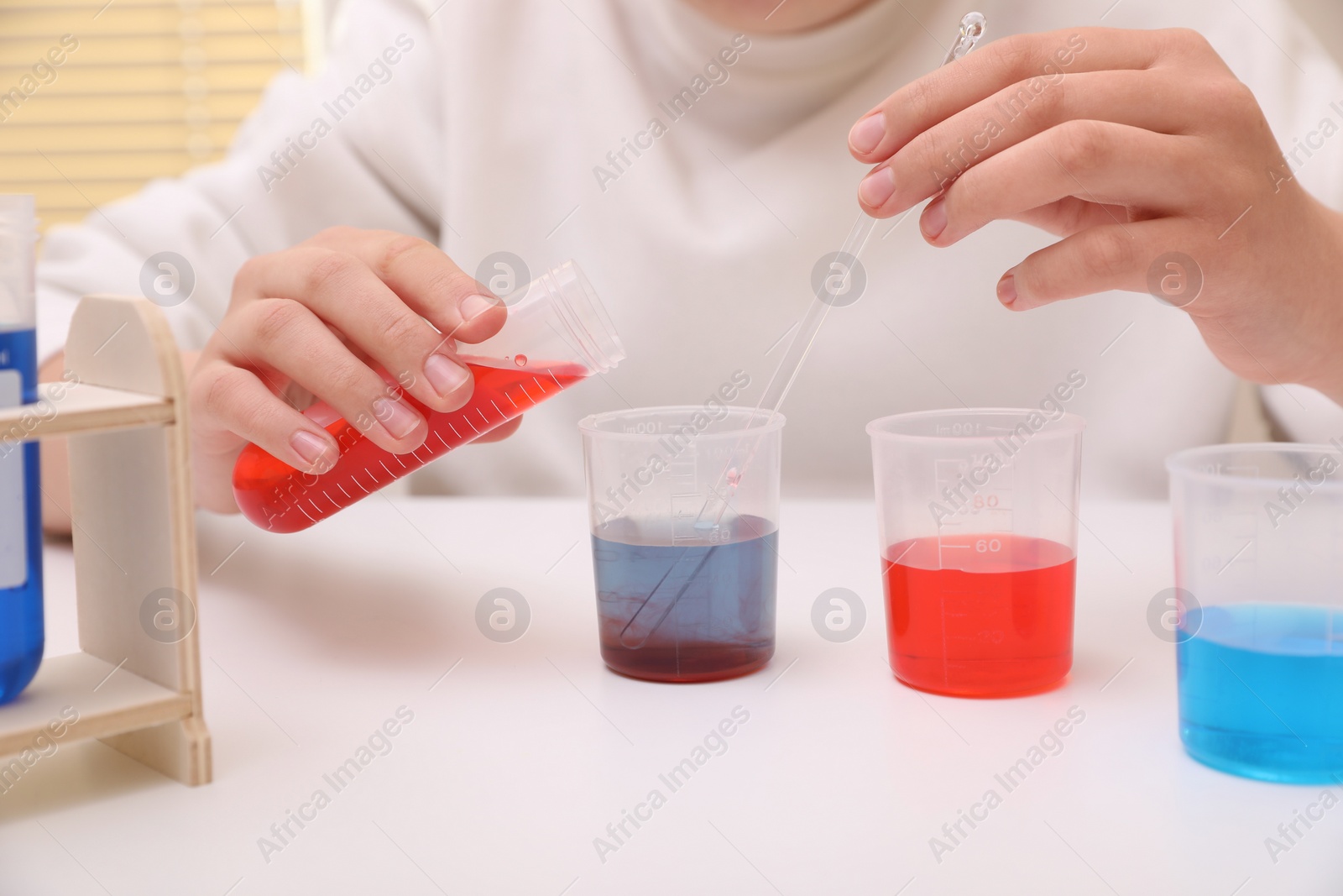 Photo of Girl mixing colorful liquids at white table indoors, closeup. Chemical experiment set for kids