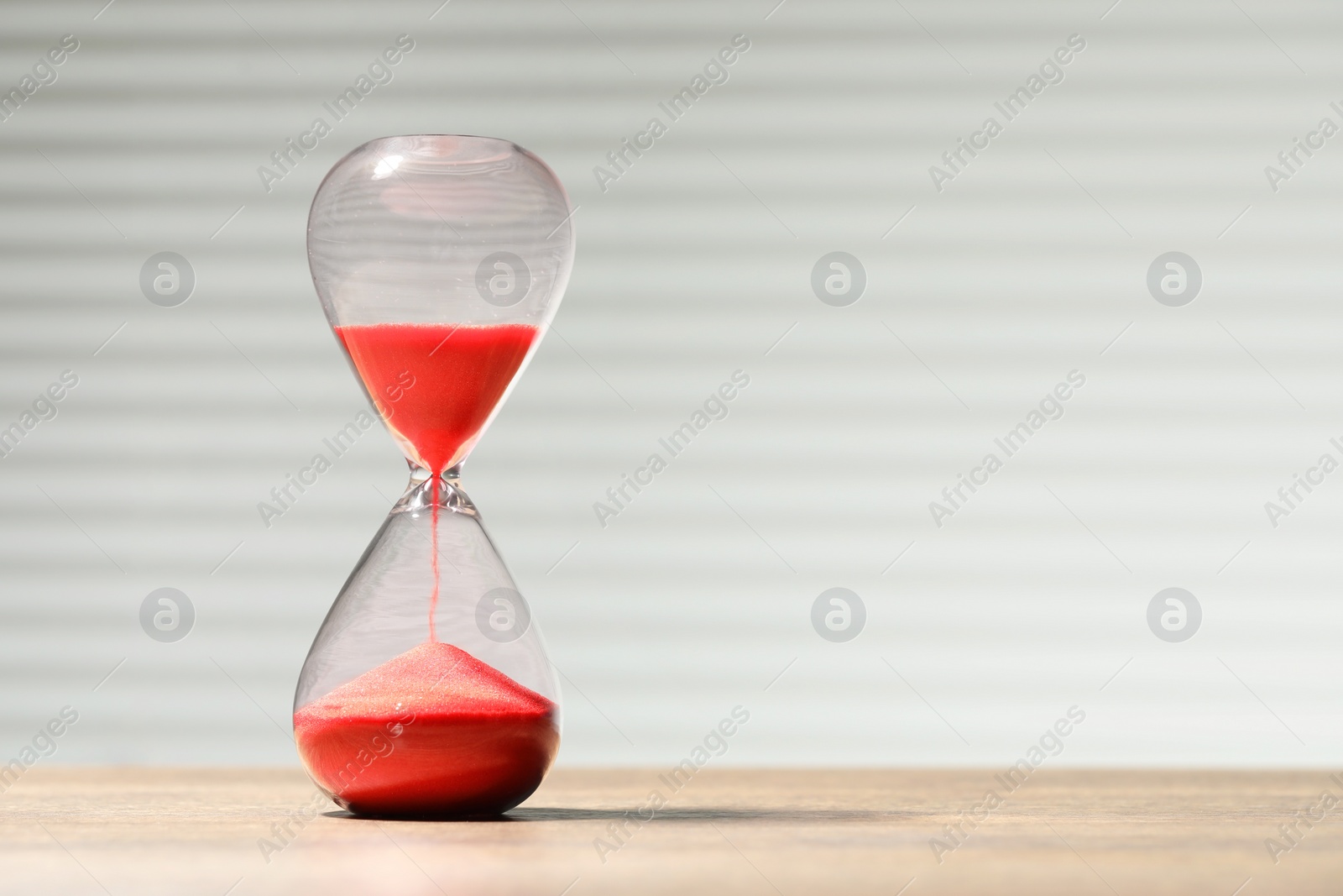 Photo of Hourglass with red flowing sand on wooden table against light background, space for text