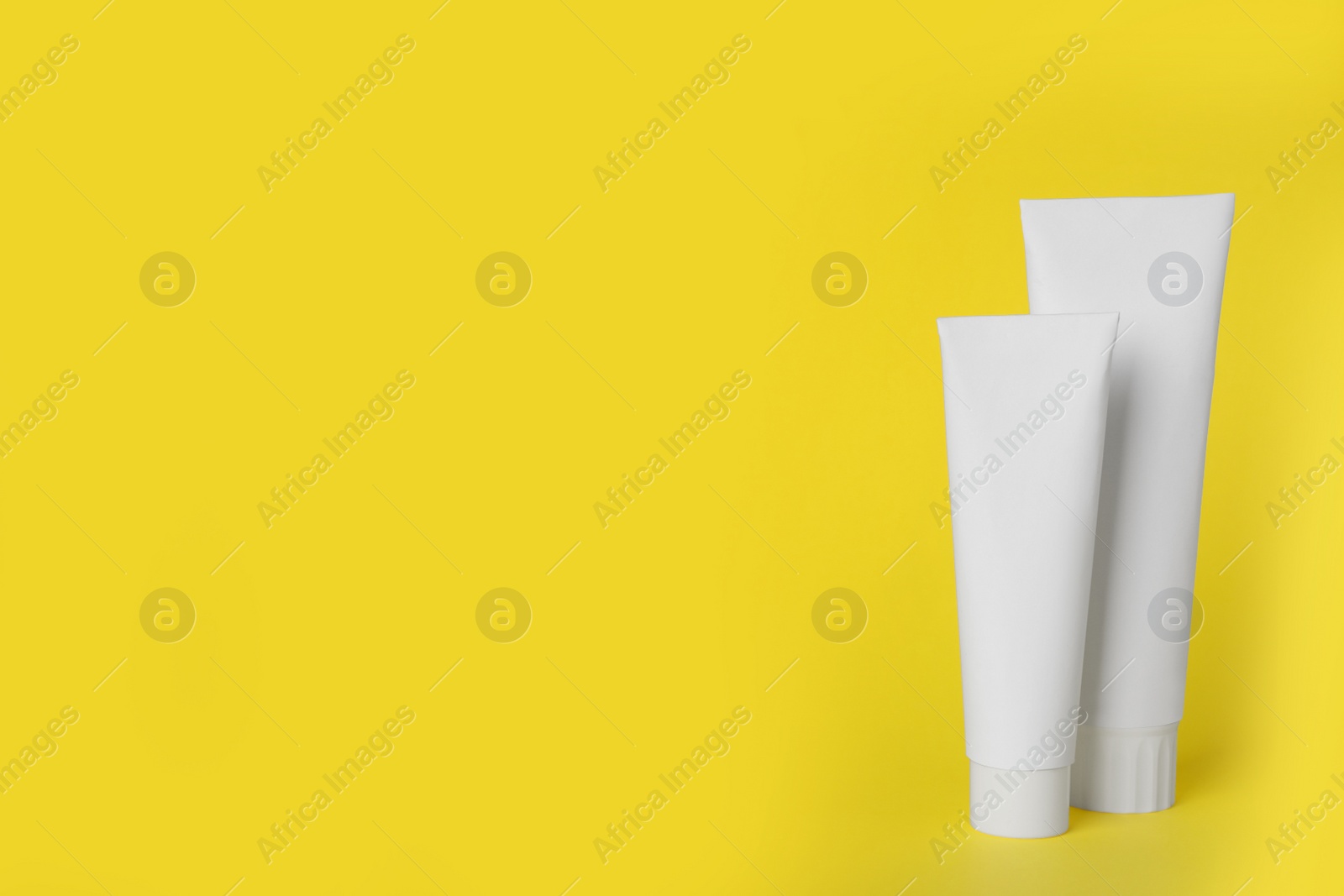 Photo of Blank tubes of toothpaste on yellow background. Space for text