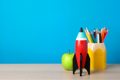 Photo of Bright toy rocket and school supplies on wooden desk. Space for text