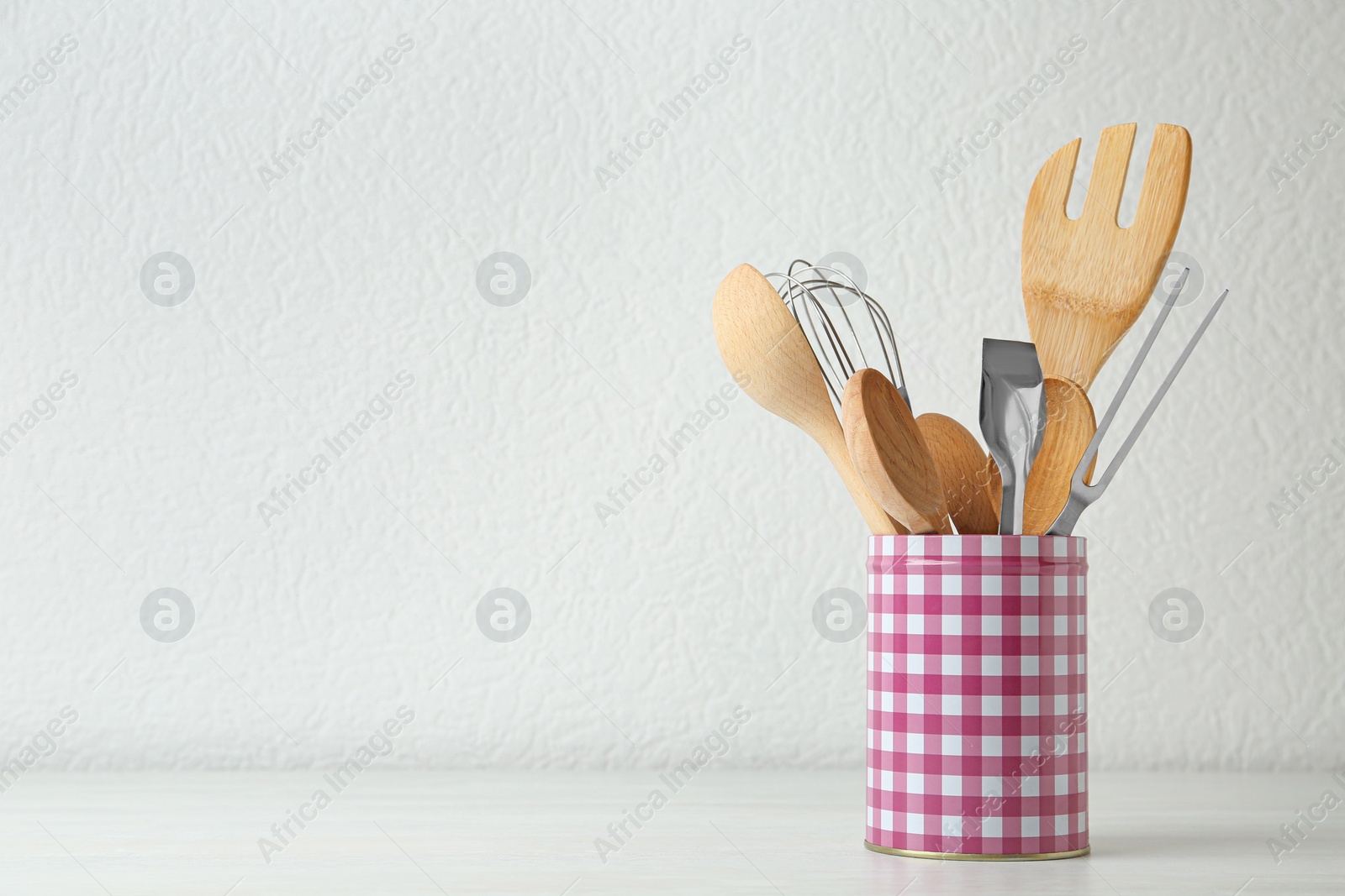 Photo of Set of kitchen utensils in stand on wooden table near light wall. Space for text