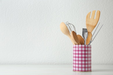 Set of kitchen utensils in stand on wooden table near light wall. Space for text