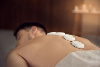 Man receiving hot stone massage in spa salon, closeup