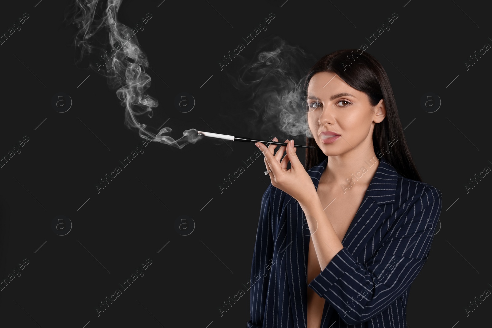 Photo of Woman using long cigarette holder for smoking on black background