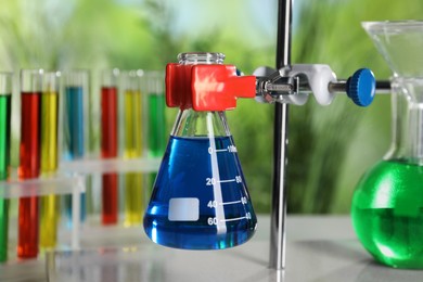 Photo of Retort stand and laboratory flask with liquid on table against blurred background, closeup