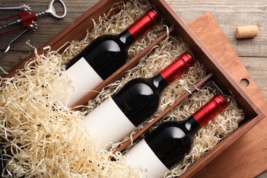 Photo of Box with wine bottles, corkscrew and cork on wooden table, flat lay