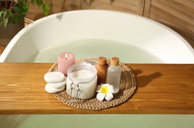 Photo of Wooden tray with spa products, stones and burning candle on bath tub in bathroom