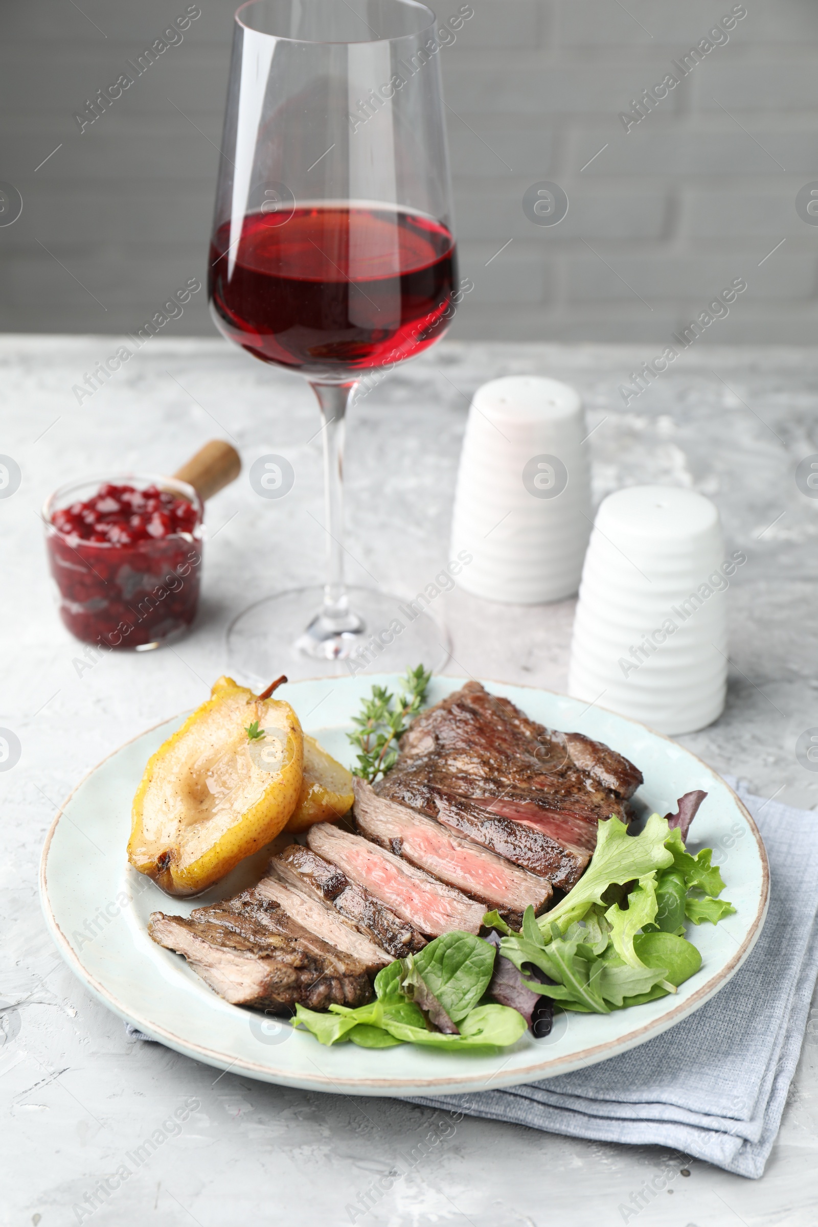 Photo of Delicious roasted beef meat, caramelized pear and greens served on light table