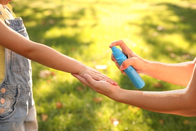 Mother applying insect repellent onto girl's hand in park, closeup