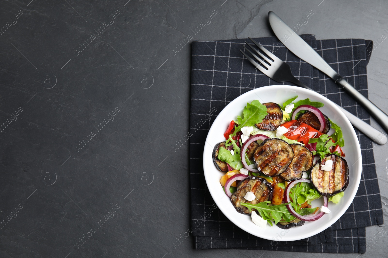 Photo of Delicious salad with roasted eggplant, cheese and arugula served on black table, flat lay. Space for text