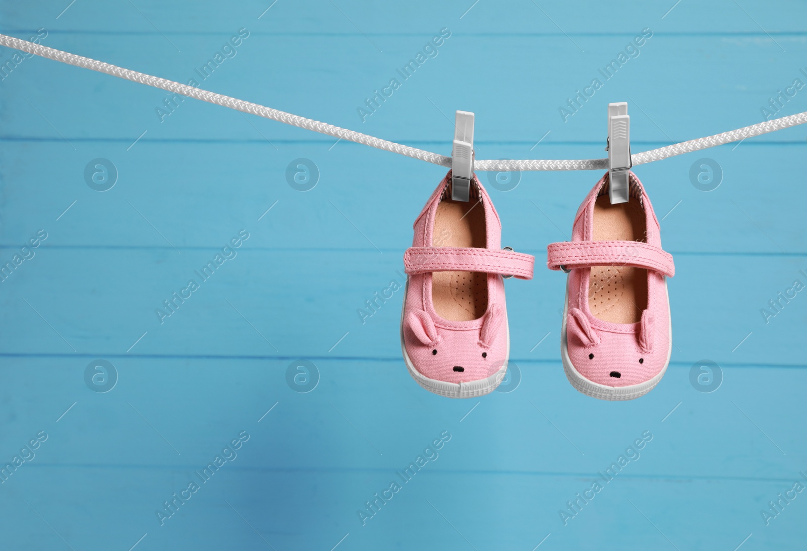 Photo of Pink baby shoes drying on washing line against light blue wooden wall. Space for text