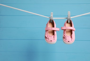 Photo of Pink baby shoes drying on washing line against light blue wooden wall. Space for text