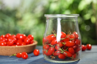 Photo of Glass jar with fresh goji berries on blue wooden table against blurred background. Space for text