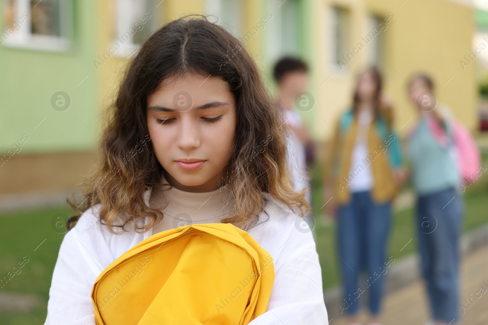 Photo of Teen problems. Lonely girl standing separately from other students outdoors