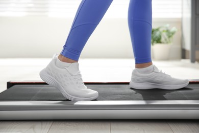 Photo of Sporty woman training on walking treadmill indoors, closeup