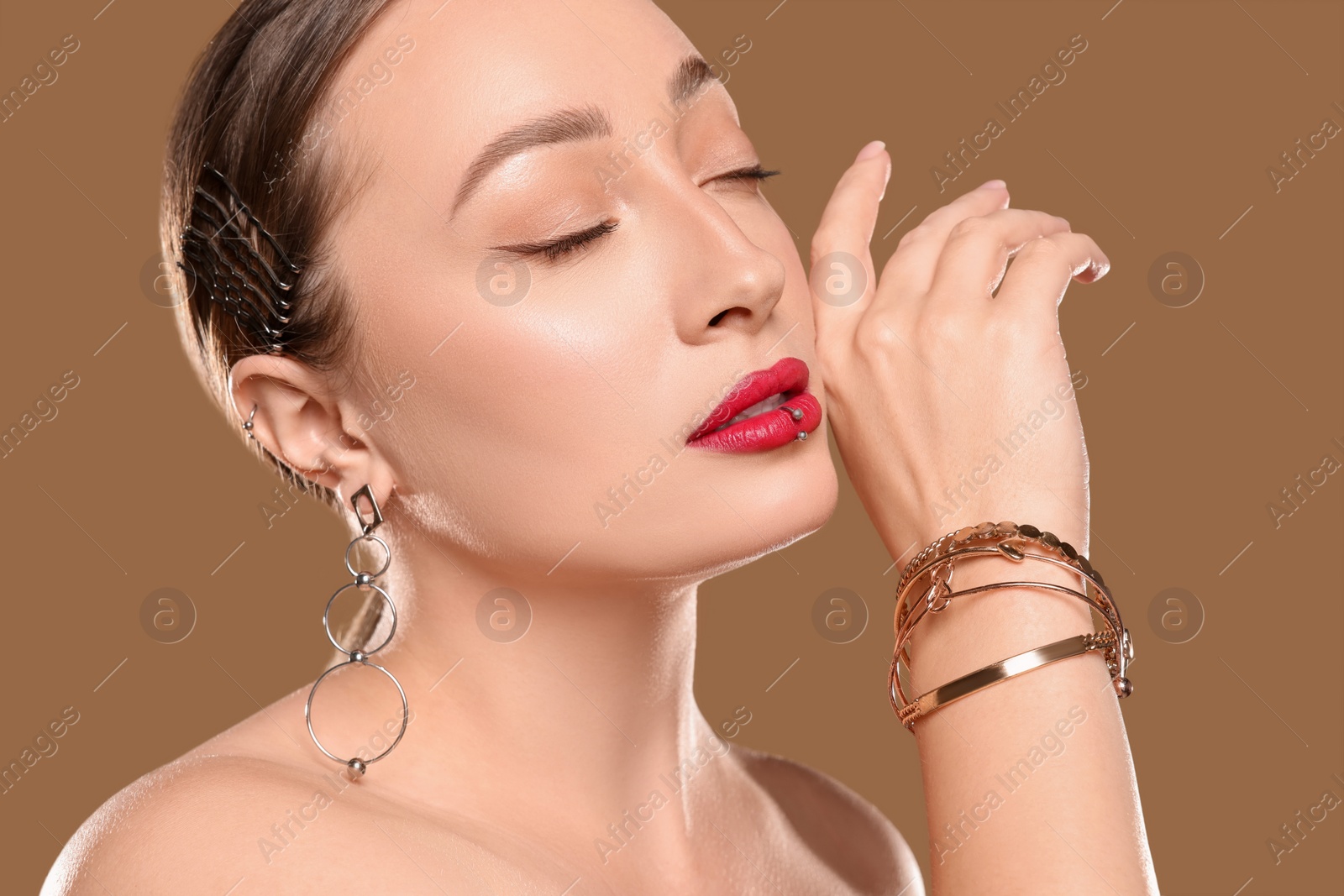 Photo of Young woman with lip and ear piercings on light brown background