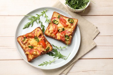 Tasty pizza toasts and fresh arugula on light wooden table, flat lay