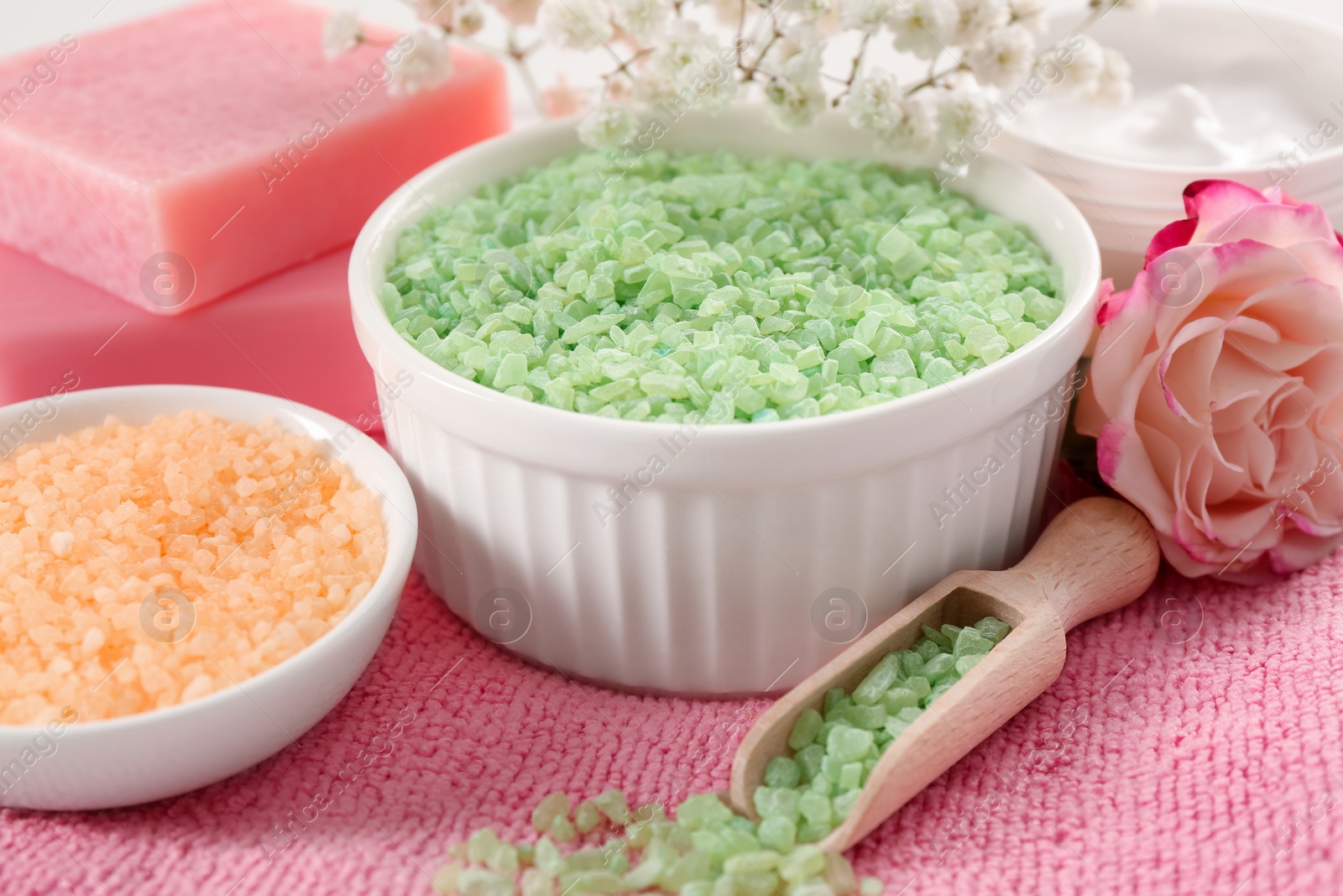 Photo of Bowls with sea salt, beautiful rose and soap bars on pink towel, closeup