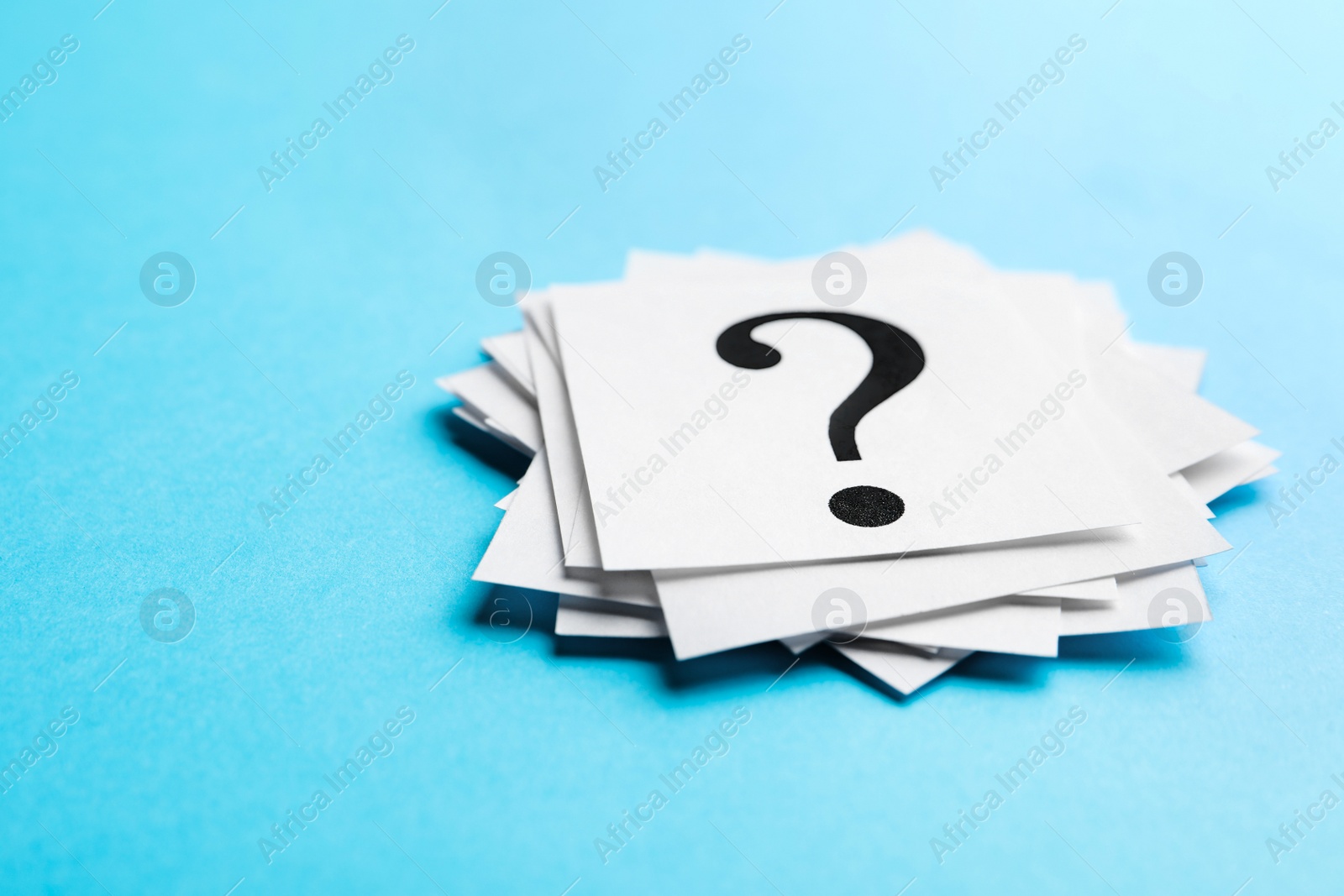 Photo of Heap of paper notes with question marks on light blue background, closeup