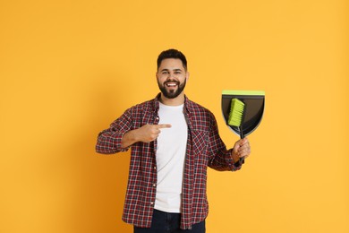 Young man with broom and dustpan on orange background