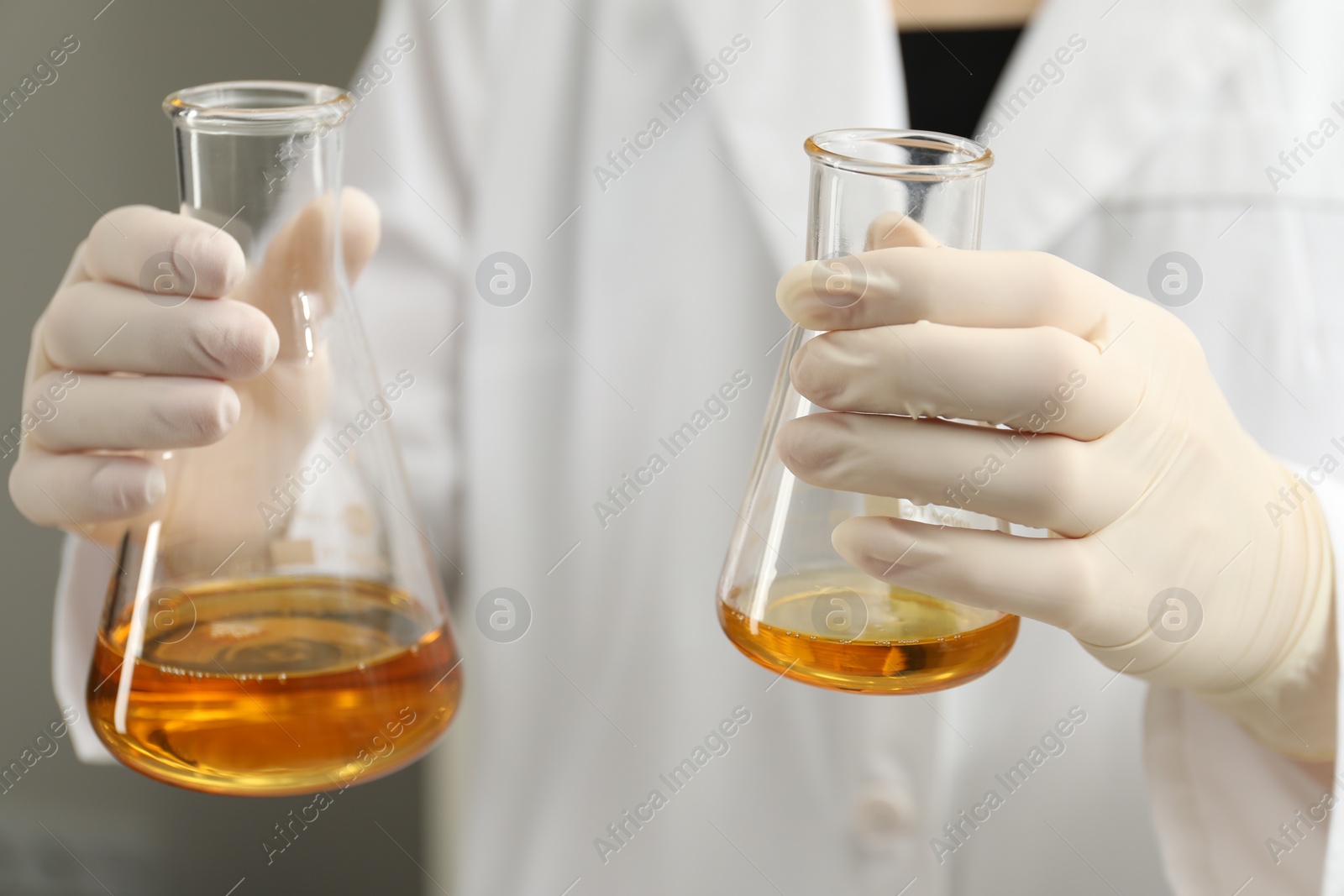 Photo of Laboratory worker holding flasks with orange crude oil, closeup