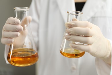 Laboratory worker holding flasks with orange crude oil, closeup