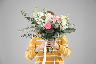 Woman covering her face with bouquet of beautiful flowers on grey background