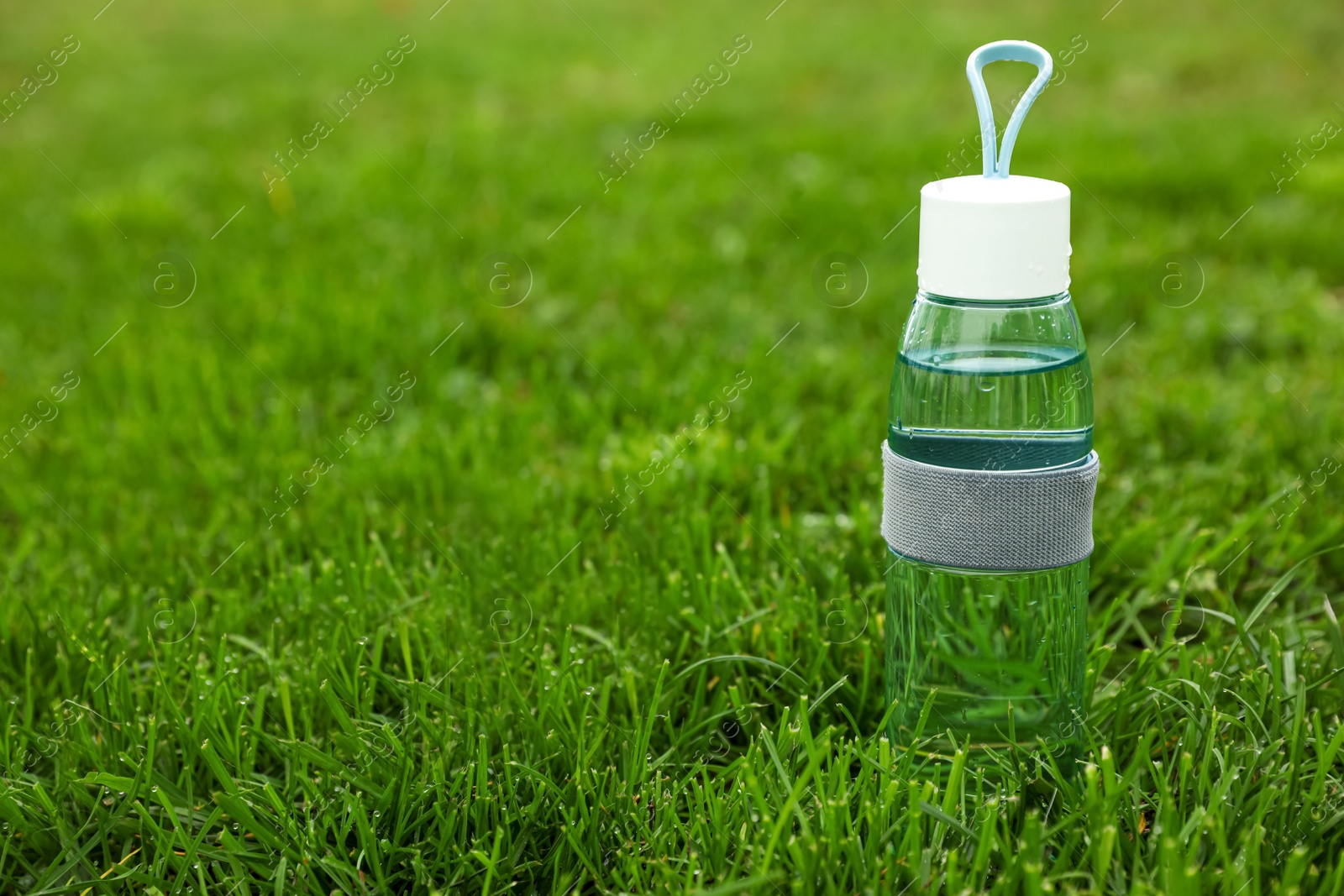 Photo of Glass bottle of fresh water in green grass, space for text