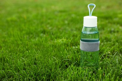 Glass bottle of fresh water in green grass, space for text