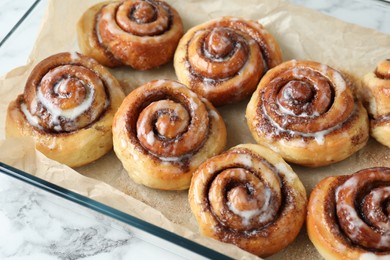 Photo of Baking dish with tasty cinnamon rolls on white marble table, closeup