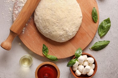 Pizza dough, products and rolling pin on gray textured table, flat lay