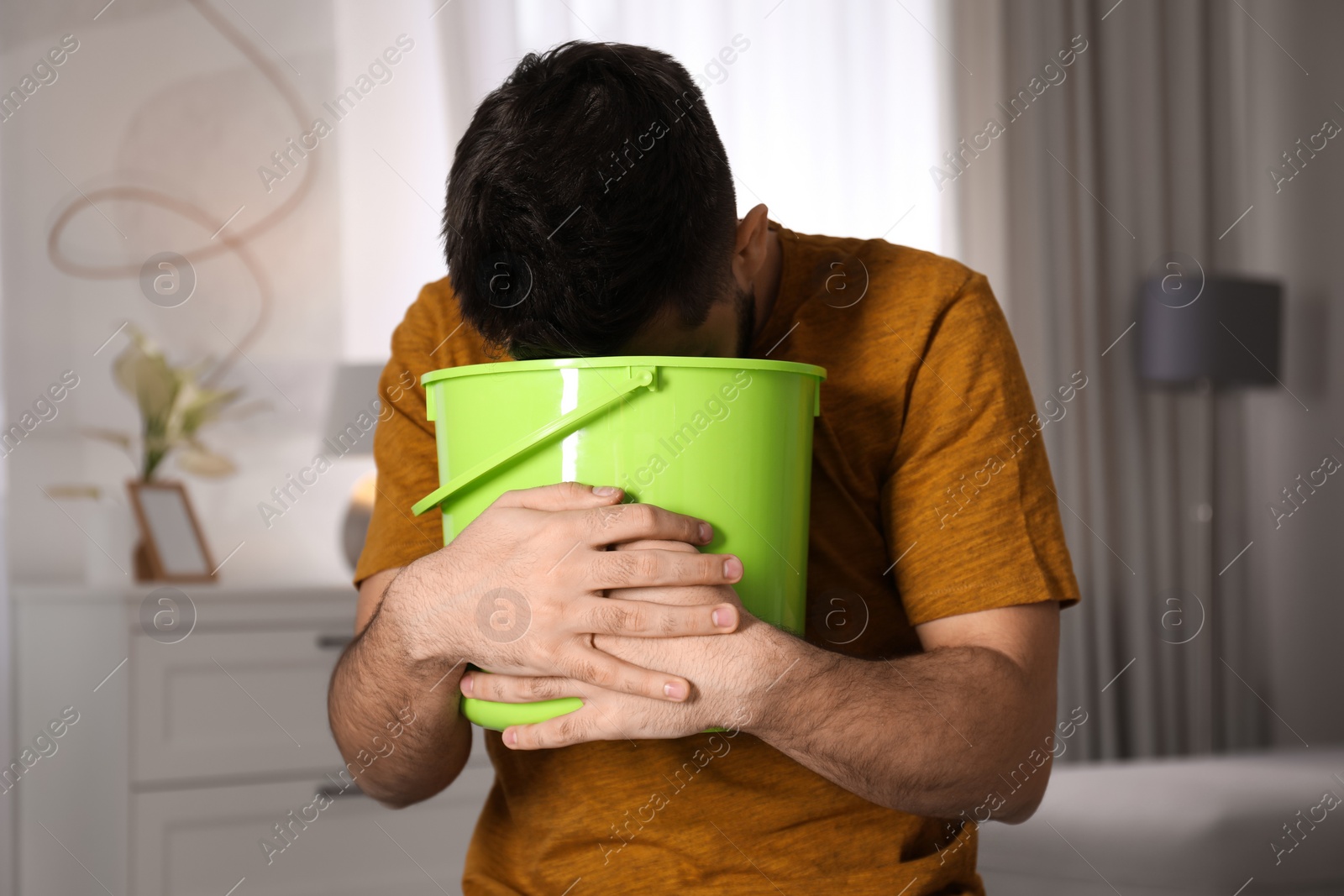 Photo of Young man with bucket suffering from nausea at home. Food poisoning