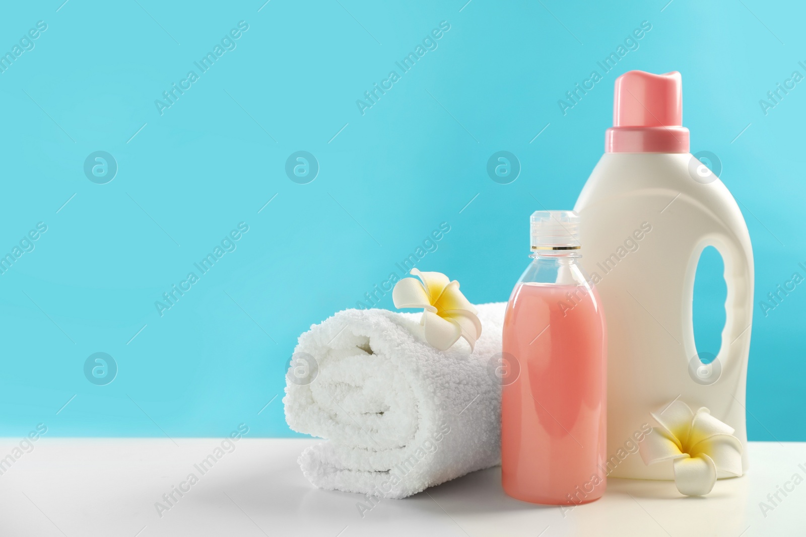 Photo of Bottles of laundry detergents, towel and plumeria flowers on white table. Space for text