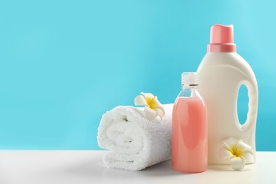 Bottles of laundry detergents, towel and plumeria flowers on white table. Space for text
