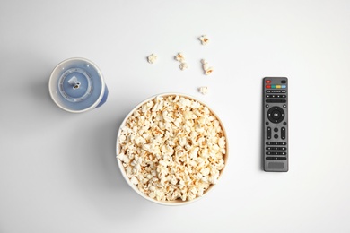 Bucket with popcorn, cup of beverage and TV remote on white background, top view. Watching cinema