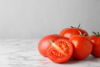 Photo of Fresh ripe whole and cut tomatoes on white marble table. Space for text