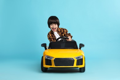 Photo of Little child driving yellow toy car on light blue background
