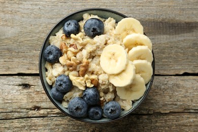 Photo of Tasty oatmeal with banana, blueberries and walnuts served in bowl on wooden table, top view